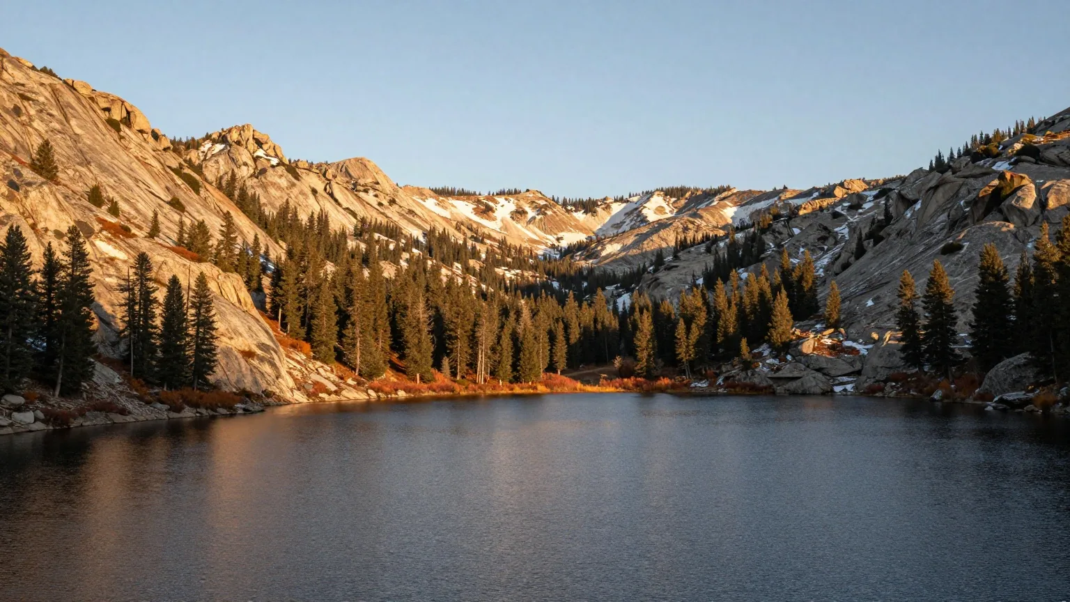 Donner Lake in der Sierra Nevada im Herbst, dunkles Wasser zwischen Granithängen und Kiefern, erster Schnee auf den Gipfeln am Pass im warmen Nachmittagslicht
