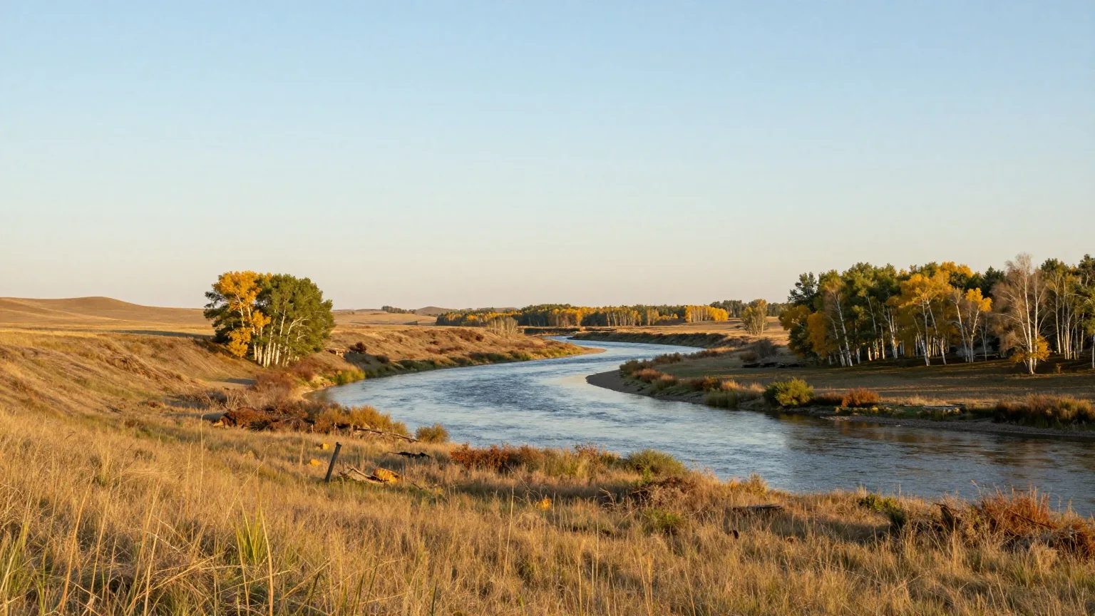 Breites Flusstal in der Prärie von Saskatchewan mit grasbewachsenen Ufern und Espenhainen im Licht des späten Nachmittags
