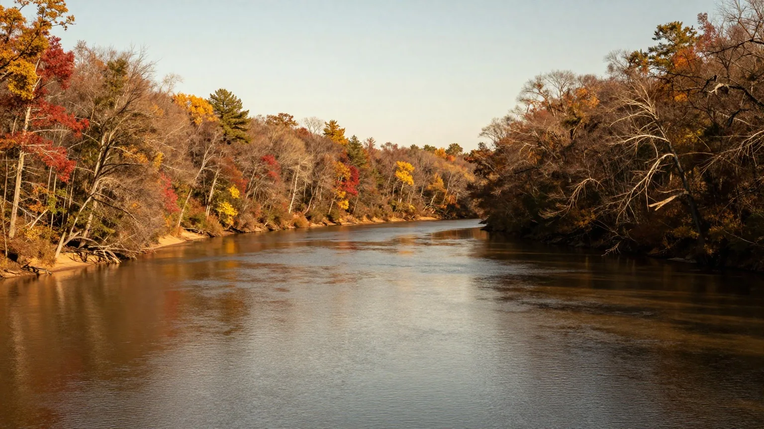 Ein Fluss beschreibt eine weite Schleife durch bewaldete Hügel im Herbst, Laubbäume am Ufer im warmen Licht der späten Nachmittagssonne