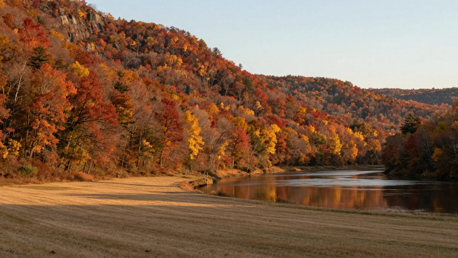 Tal eines Flusses im Westen New Yorks mit bewaldeten Hängen in Rot und Gold, Wiesen in der Talsohle und ruhigem Wasser im Licht der späten Nachmittagssonne