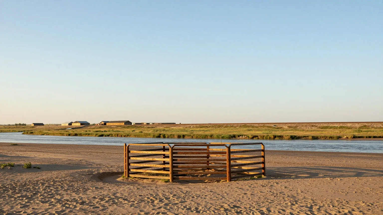 Weite, flache Prärie am Arkansas River im Licht der späten Nachmittagssonne, im Vordergrund ein Holzpferch für Rinder, in der Ferne niedrige Holzhäuser und ein Bahndamm