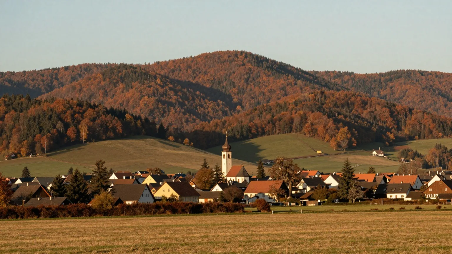 Bewaldete Hügel des Sauerlands über einem Dorf mit Kirchturm im Tal, im warmen Licht des späten Nachmittags