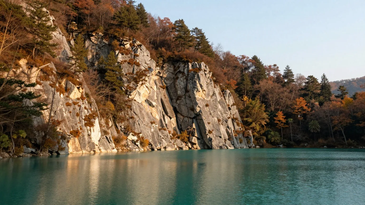 Türkisgrüner, stiller See zwischen steilen Kalkfelsen mit dichtem Wald in ersten Herbstfarben, warmes Nachmittagslicht